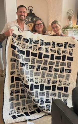 Customer's Dream Weaving Arabesque quilt held up by three people in a home living room.