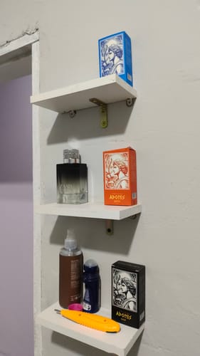 Customer's Kit Adonis perfume boxes and fragrance bottle displayed on three white wall shelves.