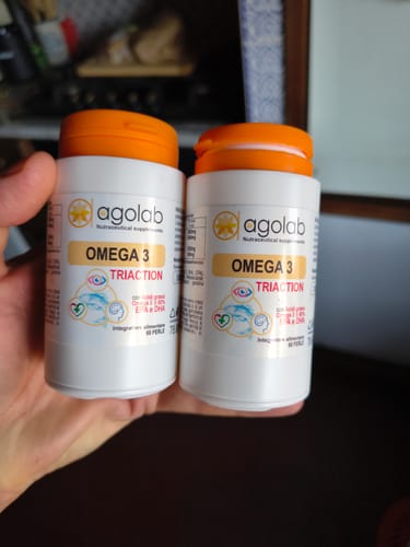 Customer's hand holding two white bottles of 3 Conf. Omega 3 with orange caps.