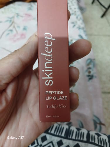 Customer's hand holding the slender, dark brown box of Skindeep Peptide Lip Glaze in Teddy Kiss shade.