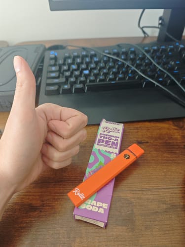 Reviewer's hand giving a thumbs up next to an orange Rollz THCA vape pen and its grape soda packaging.