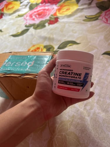 Customer's hand holding a white jar of Wellcore Micronised Creatine Monohydrate next to a delivery box.