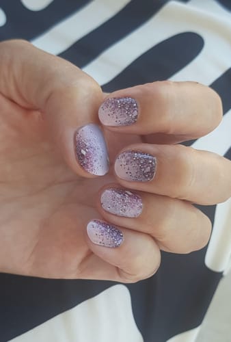 Reviewer's hand wearing Lavender Nebula UV gel nail wraps, showing a pink and purple gradient with glittery accents.